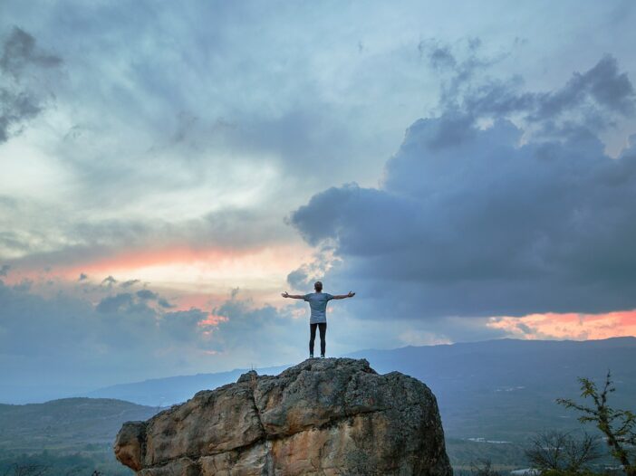 man standing on top of rock mountain during golden hour